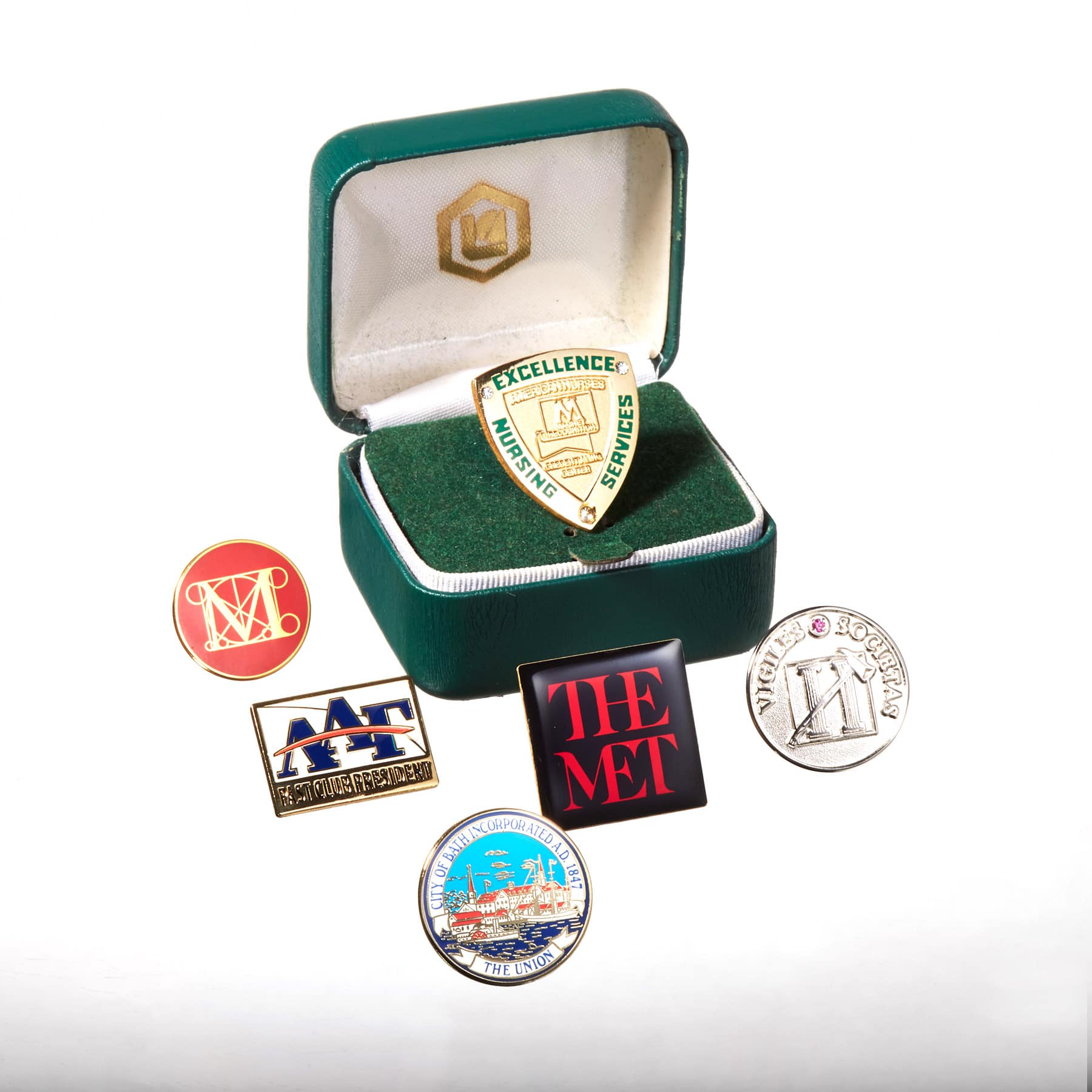 Various Embossed Award Pins in and near a green case